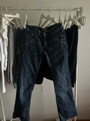 Mörkblå jeans med detaljer - Snygga mörkblå jeans med slitningar och dekorativa sömmar framtill. Jeansen har klassisk femficksdesign och coola nitar vid fickorna. Materialet är denim och passformen är rak. Perfekta för en trendig vardagslook.