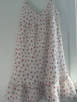 Gina Vit blommig sommarklänning med volang - Söt vit klänning med små rosa blommor. Helt ny och oanvänd. Har inte kommit till användning, säljer därav❤️❤️