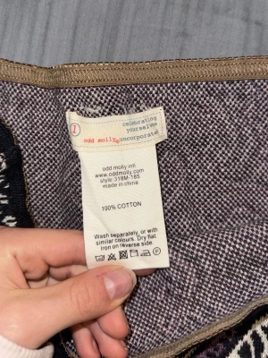 Mönstrad kjol från Odd Molly - Snygg kortkjol från Odd Molly i 100% bomull med unikt mönster i svart, lila och beige. Kjolen har en rak passform och dekorativt band upptill samt spetsdetalj nertill. Perfekt för dig som vill sticka ut med en cool och färgstark look.