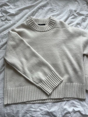 Beige stickad tröja från Gina Tricot - Mysig beige stickad tröja från Gina Tricot med bred ribbstickad kant vid hals, ärmslut och nederkant. Tröjan har en avslappnad passform och är perfekt för lager-på-lager. Enkel och stilren design som passar till det mesta.