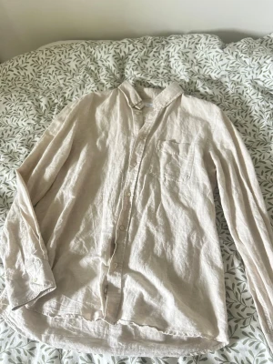 Beige linneskjorta från Zara - Säljer en stilren beige skjorta från Zara i luftigt linne. Skjortan har klassisk krage, bröstficka och knappar framtill. Perfekt för dig som gillar en avslappnad men snygg look.