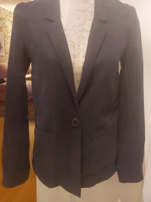 Svart kavaj med enkelknäppning - Stilren svart (lite urtvättad look)kavaj med klassisk passform och en knapp framtill. Kavajen har långa ärmar, två fickor och smala slag. Materialet är mjukt och lätt, vilket ger en bekväm känsla.