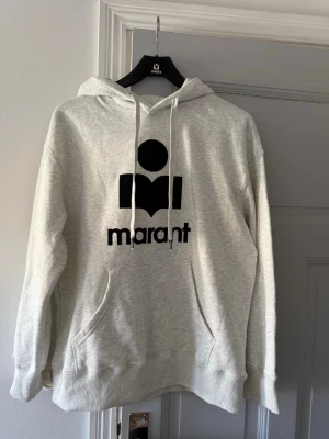 Grå hoodie från Isabel Marant - Snygg grå hoodie från Isabel Marant med stor svart logotyp på bröstet och vita dragsnören i huvan. Tröjan har en klassisk känguruficka och ribbade muddar. Helt ny, aldrig använd!!💓💓💓