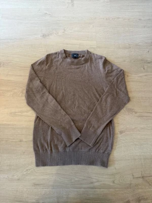 Brun stickad tröja från H&M - En stilren brun stickad tröja från H&M med rund halsringning och långa ärmar. Tröjan har ribbade muddar vid ärmslut och nederkant. Perfekt för lager-på-lager och enkel att matcha med jeans eller kjol.