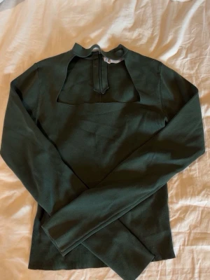 Mörkgrön ribbad långärmad topp - Trendig mörkgrön långärmad topp med ribbad struktur och unik öppen detalj vid halsen. Snygg croppad passform som passar perfekt till jeans. Materialet är mjukt och stretchigt för en bekväm känsla.