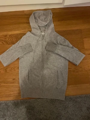 Grå hoodie i kashmir från Soft Goat - Mysig grå hoodie från Soft Goat i 100% kashmir. Tröjan har dragkedja framtill, två fickor och en stor huva. Perfekt för dig som gillar en stilren och bekväm look med exklusiv känsla. Ribbade muddar vid ärmslut och nederkant.