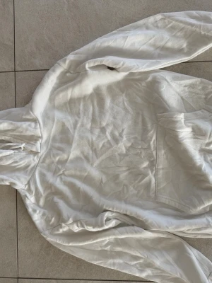 Vit hoodie med magficka - Snygg vit hoodie med klassisk huva och dragsko. Hoodien har en stor magficka framtill och är tillverkad i mjukt tyg, perfekt för en avslappnad stil. Passar dig som gillar enkel och clean design.
