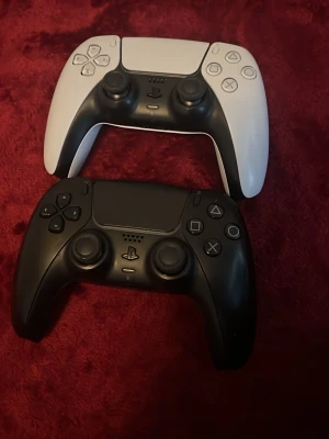 Sony DualSense PS5 handkontroller svart/vit - Två PlayStation 5 DualSense handkontroller från Sony, en i svart och en i vit. Ergonomisk design med touchpad, adaptiva triggers och inbyggd mikrofon. Tillverkade i plast med matta och blanka ytor. Perfekt för gaming på PS5.