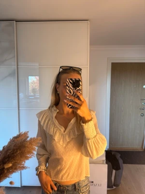 Krämvit blus från Zara - Söt krämvit blus med volangkrage och diskret prickigt mönster. Blusen har långa ärmar med smock vid ärmslut. Köpt på Zara i storlek XS