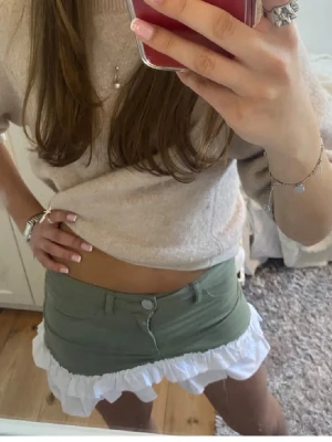 Grön minikjol med volangkant - Superfin grön kortkjol med vit volangkant nertill. Kjolen var gröna shorts från början som blev sydd till en kjol! Köpt här på Plick, superbra skick💗 bilderna är från förra ägaren! Storlek 34