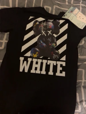 Svart Off-White t-shirt med tryck - Cool svart t-shirt från Off-White med stort grafiskt tryck på ryggen och texten 'WHITE'. Framsidan har en vit hand och texten 'Off'. Perfekt för dig som gillar streetwear och unika designer.