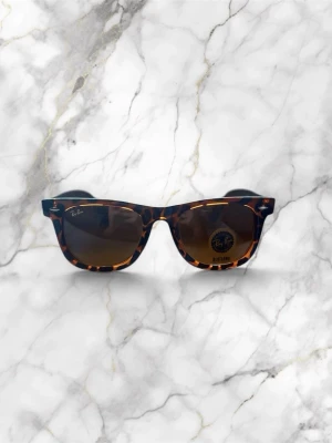 Ray-Ban Original Wayfarer RB2140-F – Tortoiseshell - Iconic Ray-Ban Wayfarer sunglasses in a striking retro tortoiseshell frame with classic brown lenses. For that perfect vintage-inspired fit. Excellent, gently pre-loved condition with no scratches or marks. Features include signature Ray-Ban logos on the lens and arm, plus bold Y2K vibes that elevate any aesthetic. Timeless statement piece for festival season, city strolls or beach days. Absolute must-have for anyone chasing that nostalgic, effortlessly cool look.