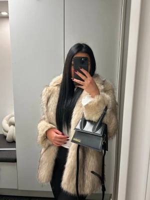 Beige fluffig pälsjacka - Säljer en snygg och fluffig beige pälsjacka med långa ärmar och rak passform. Jackan har en lyxig känsla och är perfekt för kalla vinterdagar. Materialet är fuskpäls som ger en trendig och stilren look.