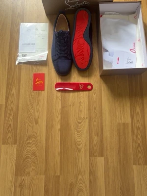 Mörkblå Christian Louboutin sneakers - Snygga mörkblå sneakers från Christian Louboutin med klassisk röd sula. Skorna har lågt skaft, ovandel i mocka och matchande blå skosnören. Kommer med originalkartong, dustbag, skohorn och äkthetskort. Perfekta för dig som gillar exklusiva detaljer och streetstyle.