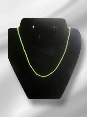 Grönt pärlhalsband i glas - Snyggt halsband med små gröna pärlor i glas. Halsbandet har en enkel och stilren design med ett silverfärgat lås. Perfekt för att ge din outfit en färgklick och passar till många olika stilar. Halsbandet är handgjord