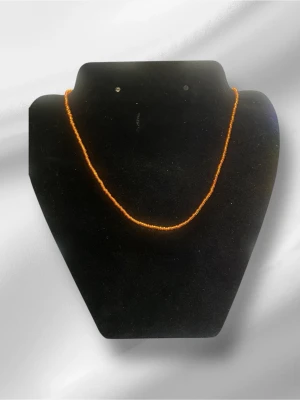 Orange pärlhalsband i enkel design - Ett smalt halsband med små orange pärlor, perfekt för att ge en färgklick till din outfit. Halsbandet har en minimalistisk och stilren form och är gjort av pärlor i plast eller glas. Passar dig som gillar färg och enkelhet.halsbandet är handgjort