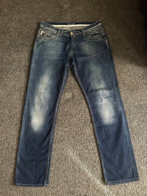 Blå raka jeans från conto bene - Snygga blå jeans från conto bene med raka ben och klassisk femficksdesign. Jeansen har slitningar och ljusare partier framtill för en cool, använd look. Tillverkade i denim med dragkedja och knapp i midjan. W34 L34