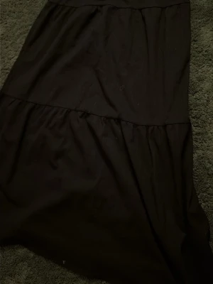 Svart långkjol från Kappahl - En svart långkjol från Kappahl med enkel och stilren design. Kjolen har en rynkad söm som ger en lätt volang-effekt och är tillverkad i ett mjukt material som känns bekvämt mot huden. Perfekt för dig som gillar en klassisk look.