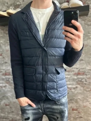 Mörkblå cardigan med kavajkrage Massimo Dutti  - Snygg mörkblå cardigan med kavajkrage och quiltad front. Jackan har två fickor med dragkedja och knappar framtill. Ärmarna är i stickat material för en cool kontrast. Perfekt för dig som vill ha en stilren men avslappnad look.