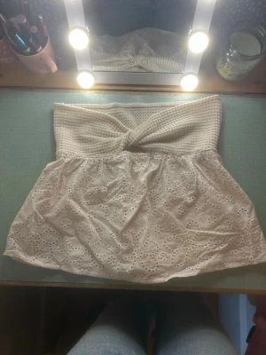 Vit broderad bandeau tubtopp - Supersöt bandeau tubtopp i vitt med virkad överdel och broderade blommor på den nedre delen. Toppen är axelbandslös och har en twistad detalj framtill. Perfekt för sommaren!! 