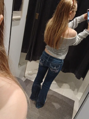 Mörkblå bootcut jeans med brodyr - Säljer ett par mörkblå bootcut jeans med vita kontrastsömmar och snygg brodyr på bakfickorna. Jeansen har låg midja och klassisk femficksmodell. Perfekta för dig som gillar en retro och avslappnad stil.