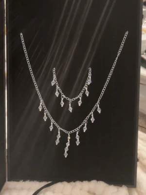 Silverfärgat halsband med kristallpärlor -  halsband och armband i silverfärgad metall med hängande klara kristallpärlor i droppform. Jag säljer även likadan men i guld