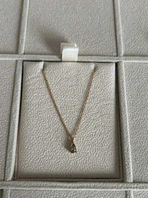 Guldhalsband med droppformad sten från Muli Collection  - Elegant halsband i guld med en tunn kedja och ett droppformat hänge med klar sten från Muli Collection. Perfekt för dig som gillar stilrena och tidlösa smycken. Passar till många olika looks och är lätt att matcha med andra accessoarer.