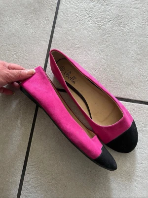 Rosa ballerinaskor med svart tå - Snygga ballerinaskor från Bella i stark rosa färg med svart tåparti. Skorna har en klassisk rundad form och är tillverkade i textilmaterial med en mjuk innersula för extra komfort. Perfekta för dig som vill ha en färgklick till din outfit.
