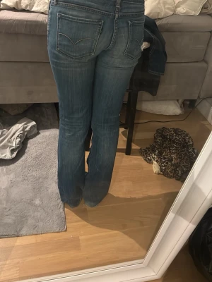 Blå bootcut jeans med slitningar - Säljer ett par blå bootcut jeans med slitningar på knäna och lätt tvättad look. Perfekta för en avslappnad och trendig stil. Få slitningar längst ner. Passar bra på mig som är 167cm och har oftast S i jeans. Lågmidjade. Hör av er vid funderingar