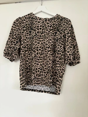 Leopardmönstrad topp med puffärm - Snygg topp med leopardmönster i beige och svart. Modellen har puffiga, halvlånga ärmar och rak passform. Perfekt för dig som vill sticka ut lite extra med ett djurmönster. Materialet känns mjukt och stretchigt. Endast tvättad och testad. Strl M