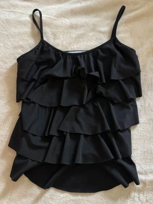 Svart volangtopp - Snyggt svart linne med flera lager volanger och smala axelband👯‍♀️Lätt att styla och passar till många sammanhang! 
