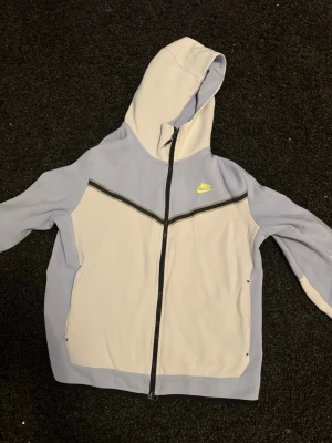 Nike hoodie i ljusblått och vitt - Stilren Nike Tech i färgerna vitt och ljus blått. Den har en liten slitning knappt märkbart men det tar ner priset såklart! ( om man stör sig på det så är det nog bara att sy igen på 5 sekunder kostar inget och man behöver ingen erfarenhet för det så sjukt bra deal!)