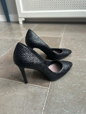 Svarta pumps från Tom Ford - Säljer ett par eleganta svarta pumps från Tom Ford med spetsig tå och hög klack. Skorna har en snygg flätad textur i läder och en stilren design som ger en lyxig känsla. Perfekta för dig som vill ha något extra till outfiten. Står strl EU 39,5 men de är små i storlek, dvs svensk 38.
