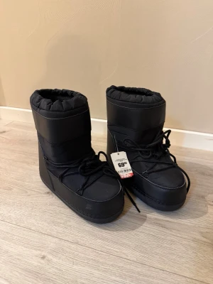 Svarta moon boots med snörning - Stilrena svarta vinterskor i storlek 37-38 från märket Duffy. med hög skaft och snörning framtill. Bootsen är varma och snygga. Perfekta för kalla vinterdagar och har en chunky, modern look. Dom är nya med prislappen kvar köpa för 70euro 