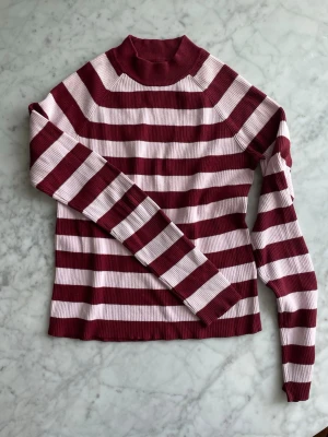 Randig tröja - Ribbad långärmad tröja från Bik Bok med breda vinröda och ros ränder. Tröjan har högre krage och är tillverkad i ett stretchigt material. Storlek L men skulle snarare säga att den är som en M.