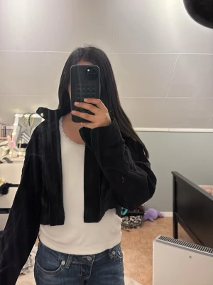 Svart cropped kofta från H&M Divided - Säljer en svart cropped kofta från H&M Divided i storlek XXS. Koftan har långa ärmar och är tillverkad i ett mjukt, ribbat material. Perfekt att slänga över en t-shirt eller linne för en avslappnad look.