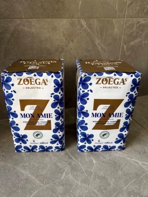 Zoégas Mon Amie jubileumskaffe(SLUTSÅLT I BUTIKER) - Två paket Zoégas Mon Amie jubileumsutgåva, mörkrost med toner av arabica och vildväxande bönor. Förpackningarna är vita med blått blommönster och guldiga detaljer. Perfekt för kaffeälskare som vill testa en unik limited edition.
