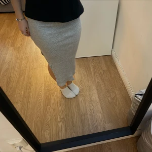 Ljusgrå långkjol med slits - Säljer en ljusgrå långkjol i mjukt material med slits på sidan. Kjolen har en enkel och stilren design som passar perfekt till både vardags och mer uppklädda tillfällen. Superskön och lätt att matcha med olika toppar.