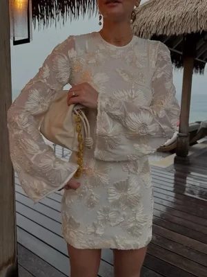 Vit blommig kortklänning med volangärm - Elegant vit kortklänning med stora blommiga broderier och transparenta volangärmar. Klänningen har rund halsringning och figurnära passform. Perfekt för sommarens alla tillfällen.