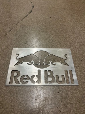 Redbull skylt  - Säljer en rektangulär metallskylt med utskuret Red Bull-motiv. Skylten har två tjurar och en cirkel i mitten samt texten 'Red Bull' i botten. Tillverkad i silverfärgad metall med borstad yta. Perfekt som dekoration för dig som gillar energidrycker eller coola loggor.
