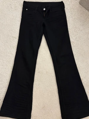 Svarta lowwaist bootcut jeans - Snygga svarta bootcut jeans med klassisk femficksdesign och normalhög midja. Jeansen har utsvängda ben och stängs med dragkedja och knapp. Perfekta för dig som gillar en retroinspirerad look och vill ha ett par jeans som sticker ut.
