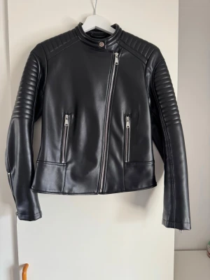 ZARA svart leather jacka, storlek S - Svart jacka med dragkedja framtill. Jackan har en krage med tryckknapp och dragkedjor vid ärmslut. Detaljerade sömmar på axlarna och ärmarna ger jackan en bikerinspirerad look. Två fickor med dragkedja framtill.  Buy shipping label or pick it up from Farsta centrum in Stockholm.