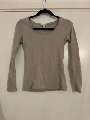 Beige långärmad topp från H&M - En enkel och stilren beige långärmad topp från H&M med rundad halsringning. Toppen är i mjuk bomull och har en slim passform som sitter snyggt på kroppen. Perfekt att matcha med jeans eller kjol.