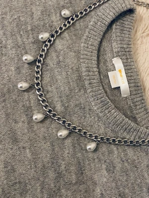 Kedjehalsband med droppformade pärlor - Snyggt halsband med silverfärgad kedja och droppformade vita pärlor som hänger längs hela kedjan. Perfekt för att ge din outfit en trendig och unik touch. Passar till många olika stilar och är lätt att matcha med andra accessoarer.