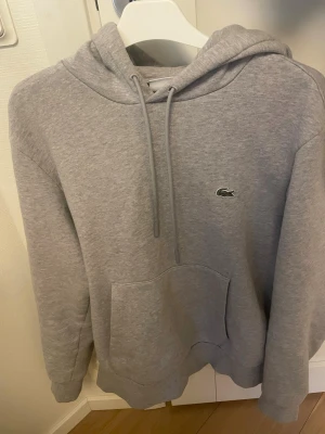 Grå hoodie från Lacoste - Tröjan är i bra skick utan några defekter. Nypris 1600 kr. Hör av dig vid frågor.