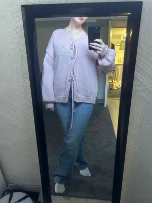 Ljusrosa stickad kofta med knytband - Säljer en ljusrosa stickad kofta med knytband framtill. Koftan har en lös passform, v-ringning och ribbade muddar vid ärmslut och nederkant. Perfekt för att skapa en avslappnad och trendig look.