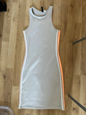 Beige ribbad klänning med neonränder - Snygg beige ribbad klänning i kort modell med ärmlös design och neonorange ränder längs sidorna. Perfekt för dig som gillar sportig och trendig stil. Figurnära passform och rund halsringning.