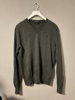 Ralph Lauren merinoull tröja grå V-neck  - Elegant grå merinoulltröja från Ralph Lauren med V-ringad hals.  Storlek: L Skick: mycket bra  Perfekt till skjorta eller för en mer stilren look.  Kan skickas eller mötas i Göteborg.