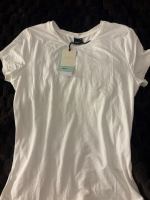 Vit t-shirt från Gina Tricot - Klassisk vit t-shirt från Gina Tricot med rund halsringning och korta ärmar. Tillverkad i mjuk bomull för extra komfort, perfekt för en enkel och stilren look. Soft touch-material som känns skönt mot huden.