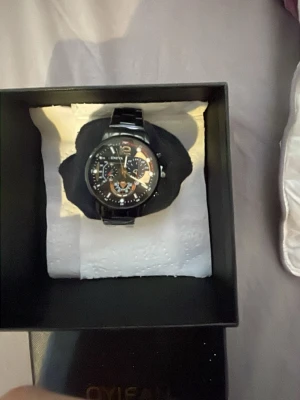 Svart metallklocka från OYIFAN - Snygg svart klocka från OYIFAN med metallarmband och detaljerad urtavla med flera små visare och siffror. Klockan har en modern design med silverfärgade och orange detaljer på urtavlan. Perfekt accessoar för dig som gillar stilrena och coola klockor.